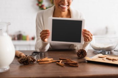Afro-Amerikan kadının tarçın çubukları ve zencefilli ekmeklerin yanında dijital tablet tutuşu. 