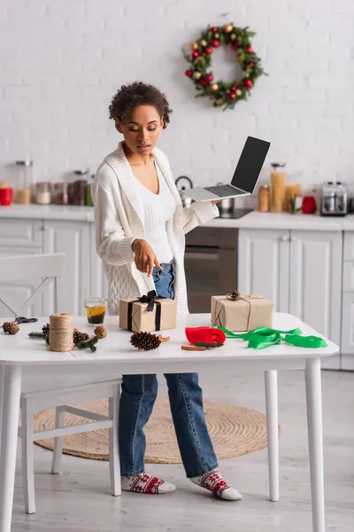 Африканська Американка Ноутбуком Вказує Подарунок Біля Христмас Декору Вдома — стокове фото