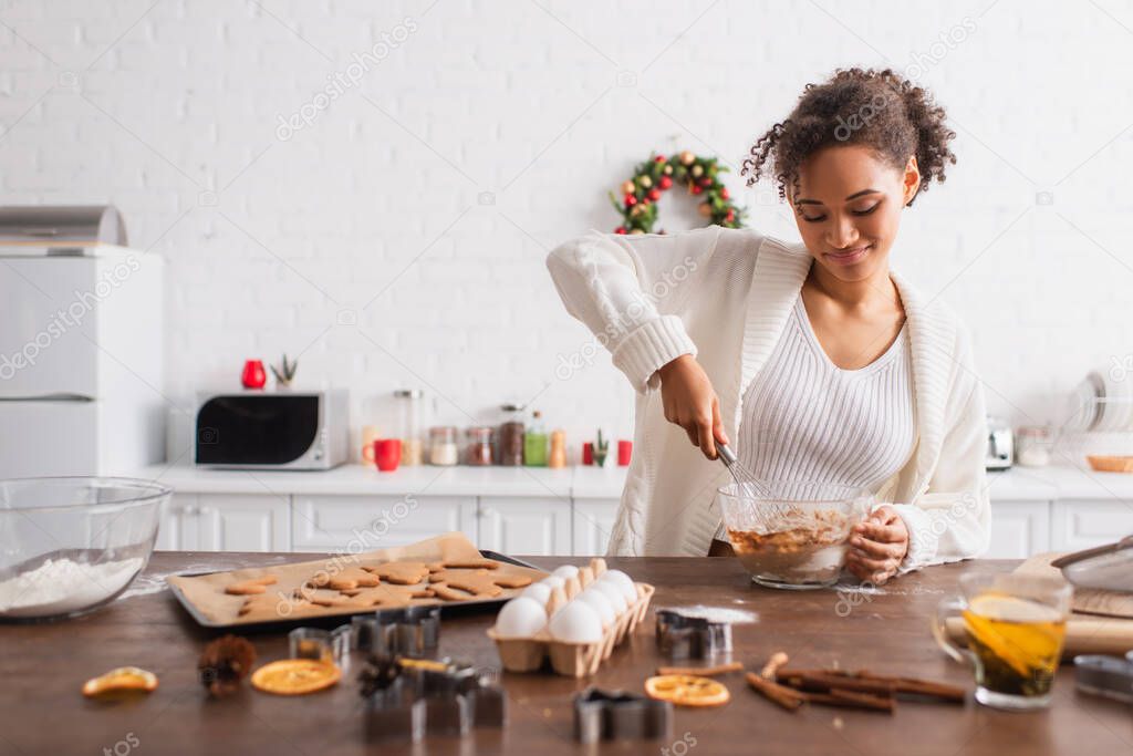 Smiling african american woman cooking near ingredients and christmas cookies in kitchen 