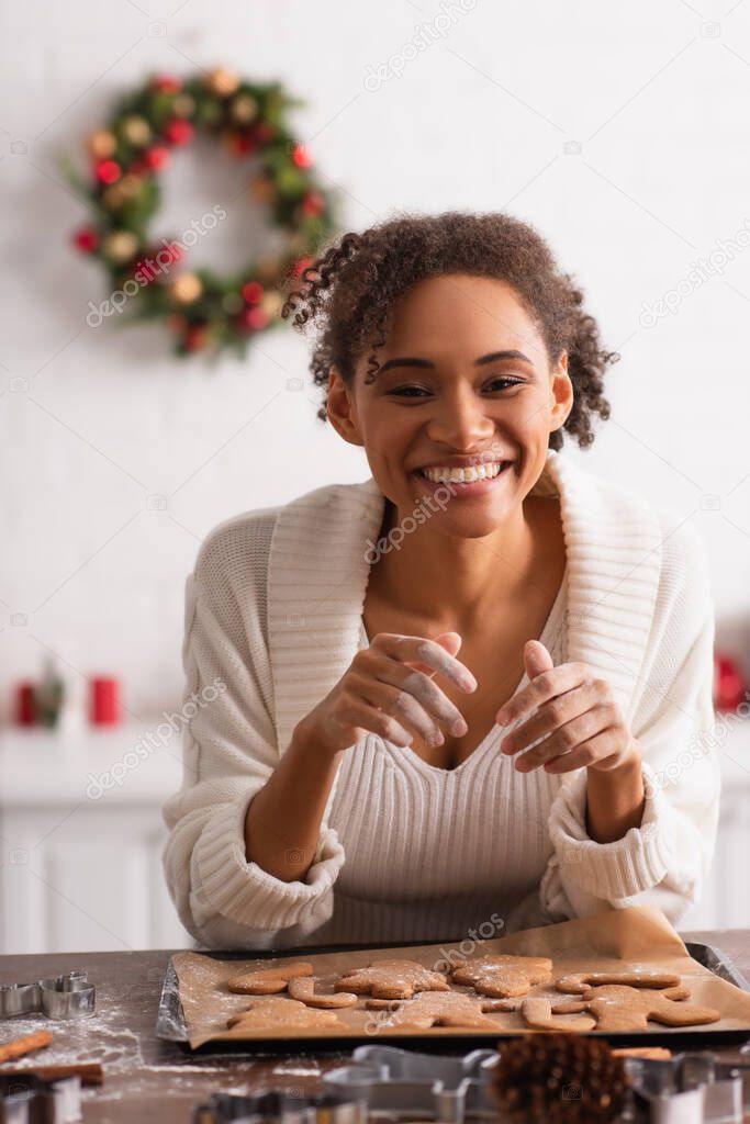 Positive african american woman looking at camera near christmas cookies in kitchen 