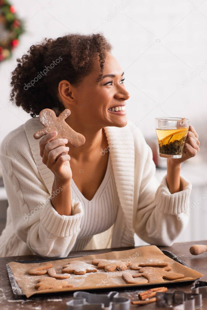 African american woman holding homemade christmas gingerbread and tea in kitchen 