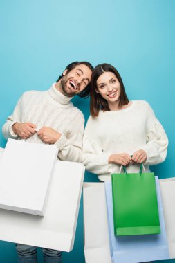Mutlu bir kadın ve alışveriş çantalı bir adam mavi kameraya bakıyor.