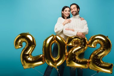 Mutlu kadın, 2022 model altın balonların yanında gülümseyen adamı kucaklıyor.