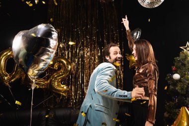 Yeni yıl partisinde zarif bir kadınla dans ederken kameraya bakan neşeli bir adam.