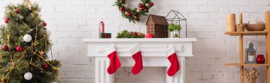 Şömine, oturma odasında askı ve noel ağacının yanında Noel çoraplarıyla süslenmiş.