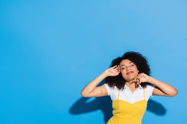 Memnun Afro-Amerikalı kadın. Elleri yüzüne yakın poz veriyor ve mavi gözleri kapalı.