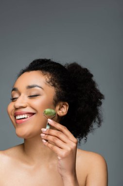 Mükemmel ciltli ve doğal makyajlı mutlu bir Afro-Amerikan kadını, yeşil tekerlekli yeşim taşıyla gri renkte izole edilmiş.