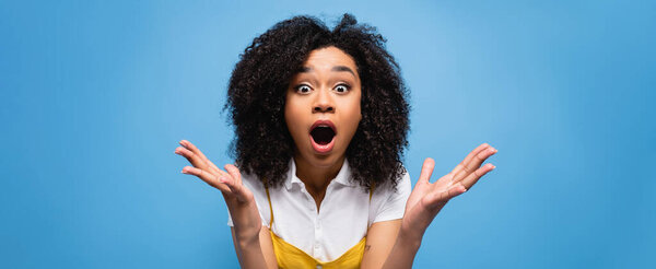 amazed african american woman showing wow gesture while looking at camera isolated on blue, banner