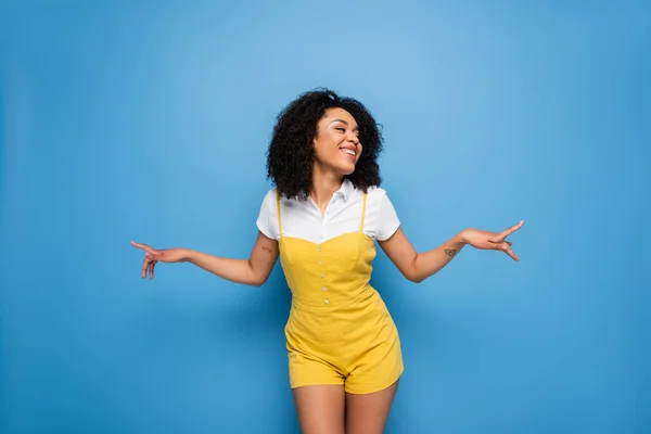 Szczęśliwy Afryki Amerykanka Kobieta Żółty Kombinezon Wskazując Palcami Niebieski — Zdjęcie stockowe