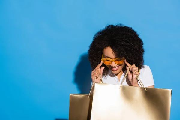 Happy African American Woman Golden Shopping Bags Adjusting Yellow Eyeglasses — Stock Photo, Image