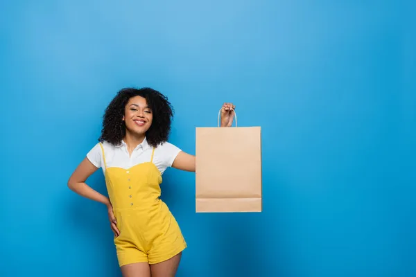 Sarı Tulumlu Neşeli Afro Amerikalı Kadın Elleri Kalçasında Alışveriş Torbası — Stok fotoğraf