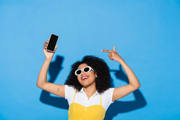 Веселая Африканская Американка Модных Солнцезащитных Очках Указывает Смартфон Чистым Экраном — стоковое фото