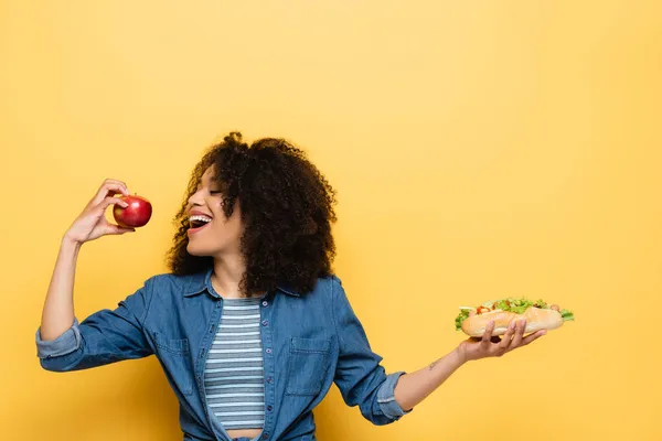 Complacida Mujer Afroamericana Mordiendo Manzana Fresca Mientras Sostiene Hot Dog —  Fotos de Stock