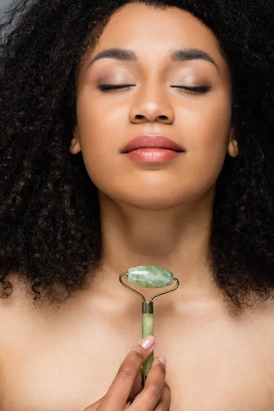 pretty african american woman with closed eyes and natural makeup holding jade roller