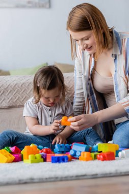 Woman playing building block with child with down syndrome on carpet in bedroom  clipart