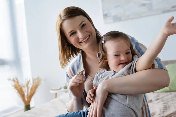 Usmívající Žena Dívá Kameru Zatímco Objímající Dceru Downovým Syndromem Posteli — Stock fotografie