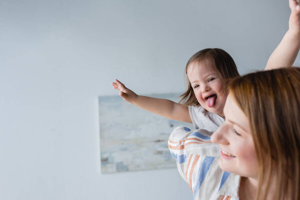 Ребенок с синдромом Дауна торчит язык рядом с размытой матерью дома  