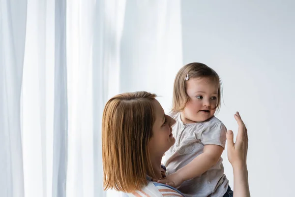 Mulher Sorridente Olhando Para Criança Com Síndrome Perto Cortinas Casa — Fotografia de Stock