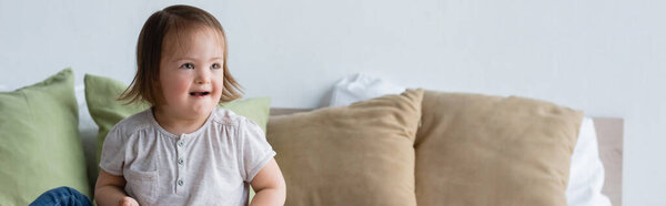 Smiling toddler girl with down syndrome looking away on bed, banner 