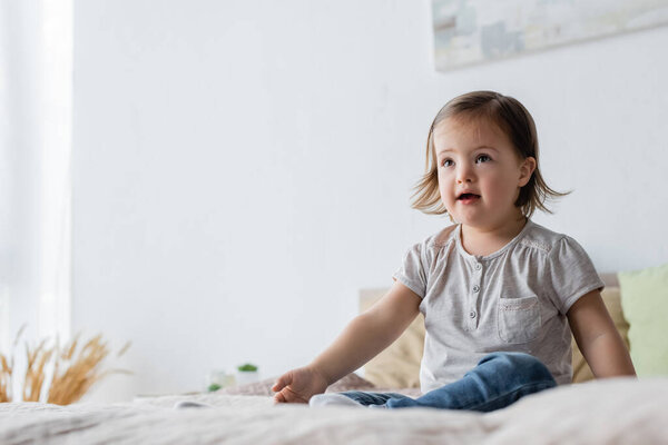 Girl with down syndrome looking away on bed at home 