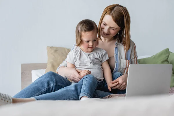 Mulher Positiva Olhando Para Criança Com Síndrome Perto Laptop Cama — Fotografia de Stock