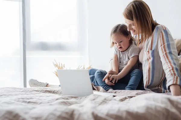 Lycklig Förälder Pekar Laptop Nära Dotter Med Ner Syndrom Sängen — Stockfoto
