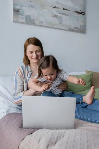 Leende Kvinna Håller Barn Med Ner Syndrom Nära Laptop Sovrummet — Stockfoto