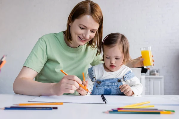 Smiling mom and daughter with down syndrome drawing in kitchen