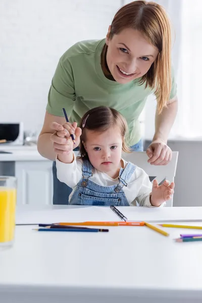 笑顔女性を見ますカメラ近くの子供とともにダウン症候群と色鉛筆 — ストック写真