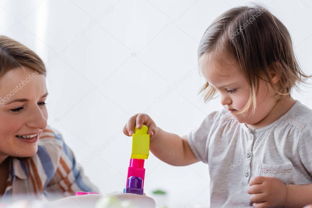 Child with down syndrome playing building blocks near mom at home 