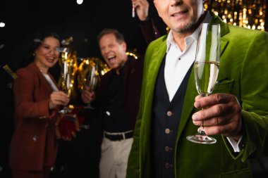 Yeni yıl partisinde elinde şampanya tutan olgun bir adam siyah arka planda bulanık ırklar arası arkadaşlar.