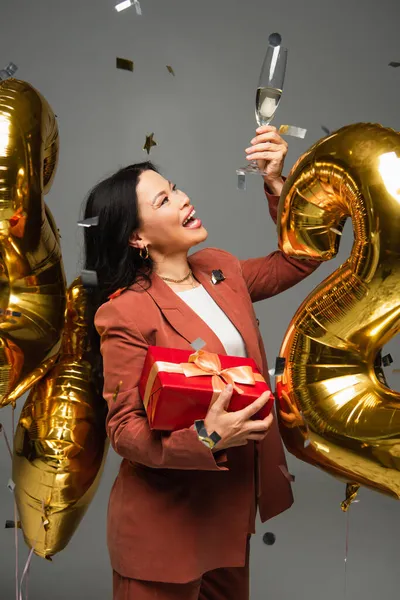 Vzrušená Asijské Žena Dárkem Při Pohledu Sklo Šampaňského Blízkosti Balónky — Stock fotografie