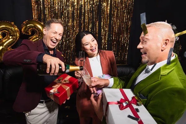 Happy Mature Man Pouring Champagne Glasses Interracial Friends Gifts Confetti — Stock Photo, Image