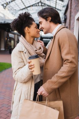 Kahveli mutlu Afro-Amerikan kadının yan görüntüsü ellerinde alışveriş poşetleri olan mutlu bir erkek arkadaşın yanına gidiyor.