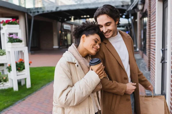 幸せなアフリカ系アメリカ人女性でコーヒーを飲みながら買い物袋を持って彼氏にもたれかかる — ストック写真