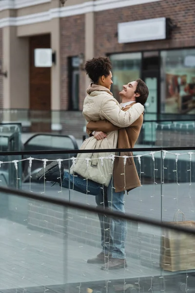 Cheerful Man Lifting African American Girlfriend Shopping Mall — Stock Photo, Image