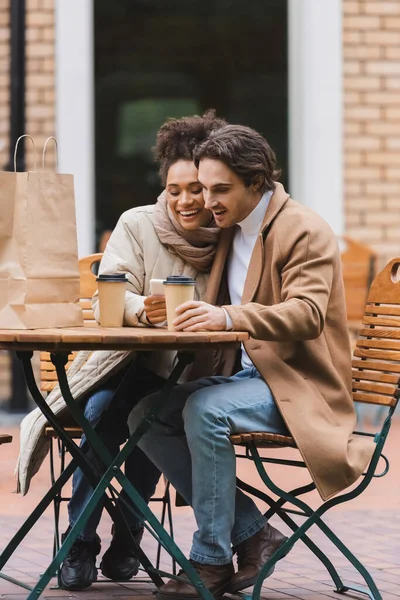 Mujer Afroamericana Complacida Sosteniendo Teléfono Inteligente Cerca Novio Con Taza —  Fotos de Stock