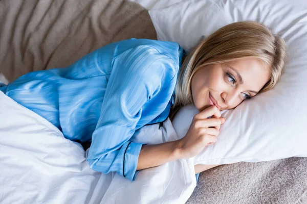 top view of cheerful blonde woman lying on bed in bedroom