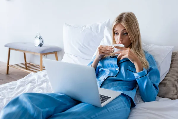 Blonde Junge Frau Schlafanzug Benutzt Laptop Und Trinkt Kaffee — Stockfoto