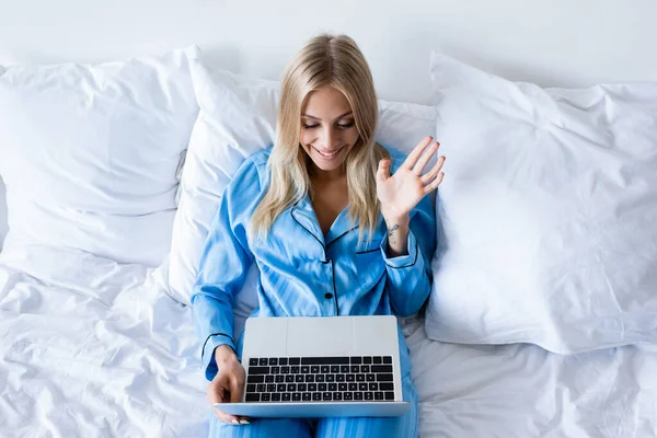 ビデオ通話中に手を振るパジャマ姿の明るい若い女性の高い角度ビュー — ストック写真
