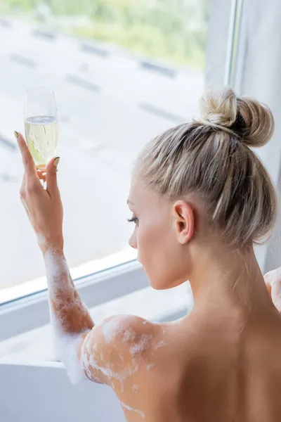 年轻的湿婆一边洗澡 一边举着香槟酒 看着窗户 — 图库照片