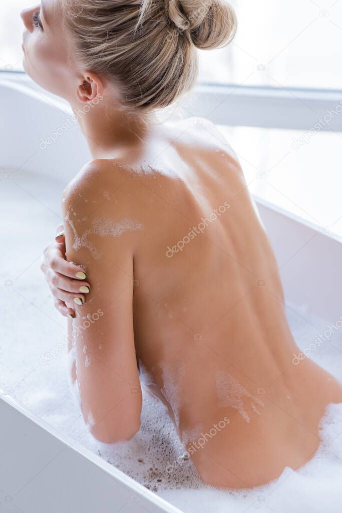 young and blonde woman with foam on body taking bath 
