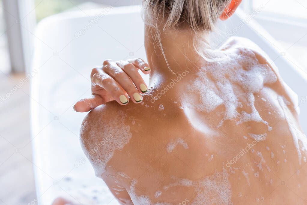 back view of young and wet woman with foam on body taking bath 