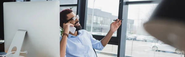 Glad Afrikansk Amerikansk Affärsman Med Penna Talar Smartphone Nära Datorn — Stockfoto