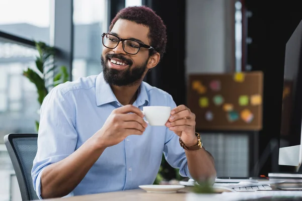 オフィスのコンピュータの近くにコーヒーカップを保持眼鏡で肯定的なアフリカ系アメリカ人ビジネスマン — ストック写真