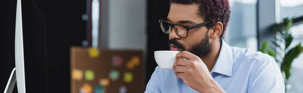 アフリカ系アメリカ人マネージャーコンピュータ バナーの近くのコーヒーカップを保持 — ストック写真