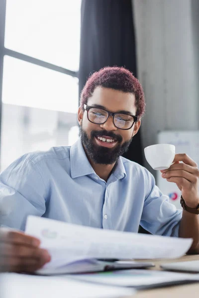 オフィスでコーヒーカップと紙を保持眼鏡で陽気なアフリカ系アメリカ人ビジネスマン — ストック写真