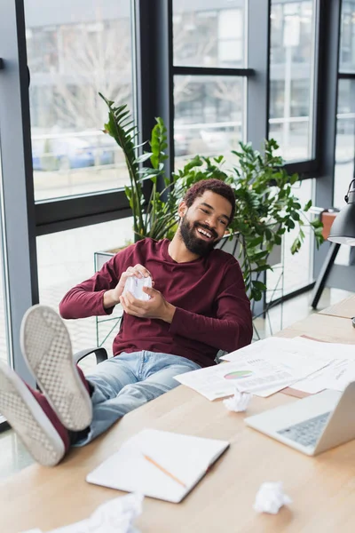 Sonriente Empresario Afroamericano Sosteniendo Papel Arrugado Cerca Computadora Portátil Oficina — Foto de Stock