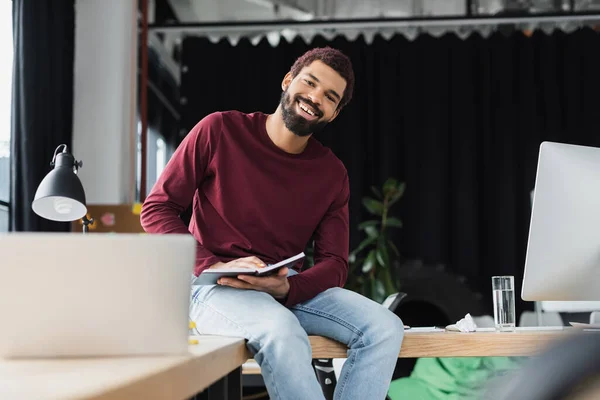 Afroamerikansk Affärsman Ler Mot Kameran Medan Håller Anteckningsbok Nära Bärbar — Stockfoto