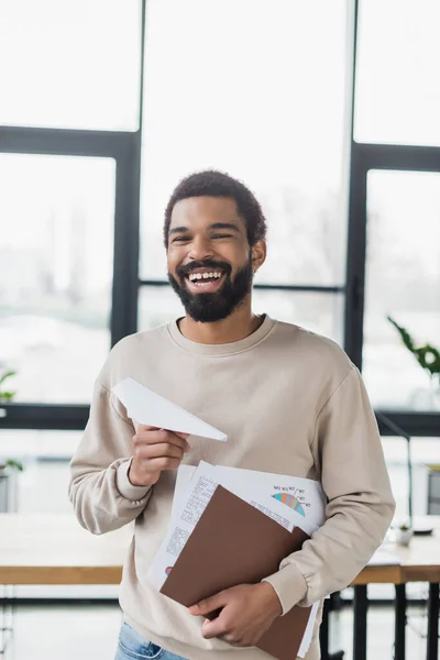Χαρούμενος Αφροαμερικάνος Επιχειρηματίας Χάρτινο Αεροπλάνο Και Έγγραφα Στο Γραφείο — Φωτογραφία Αρχείου